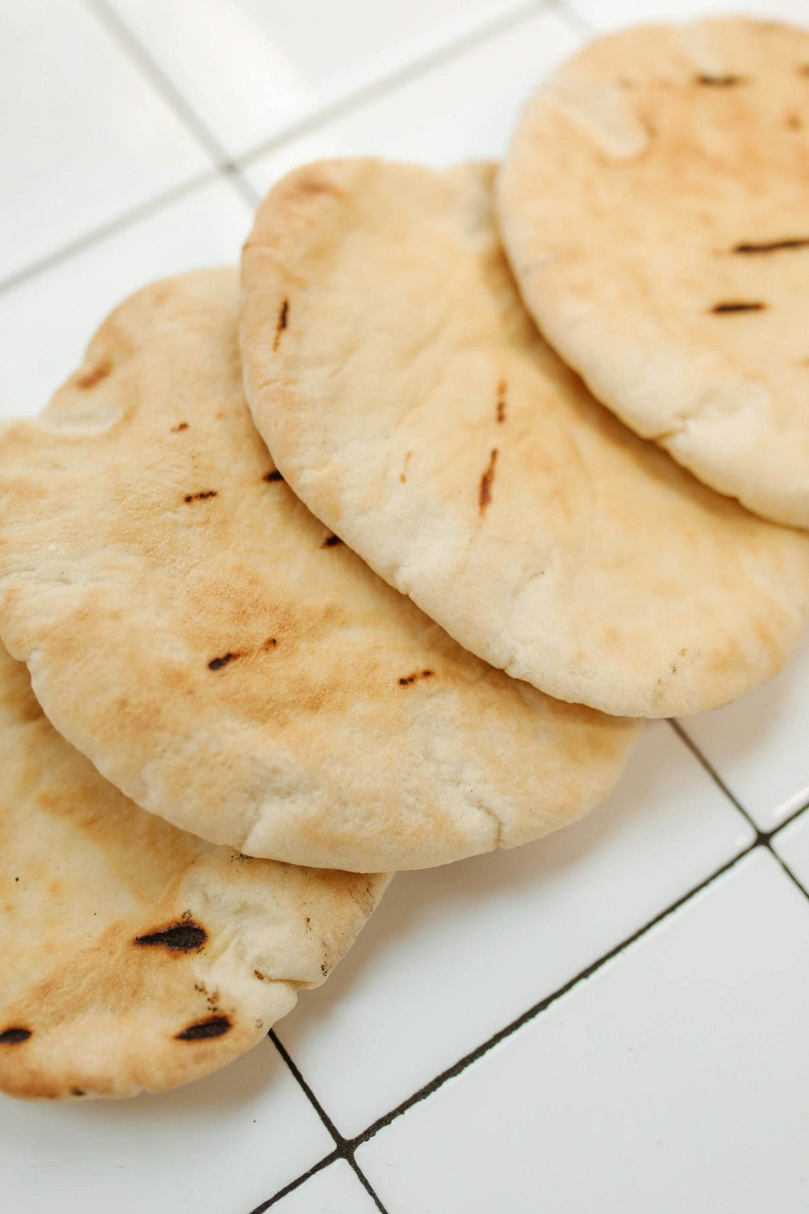Close-up of freshly baked pita bread on a white tiled background, showcasing its texture.