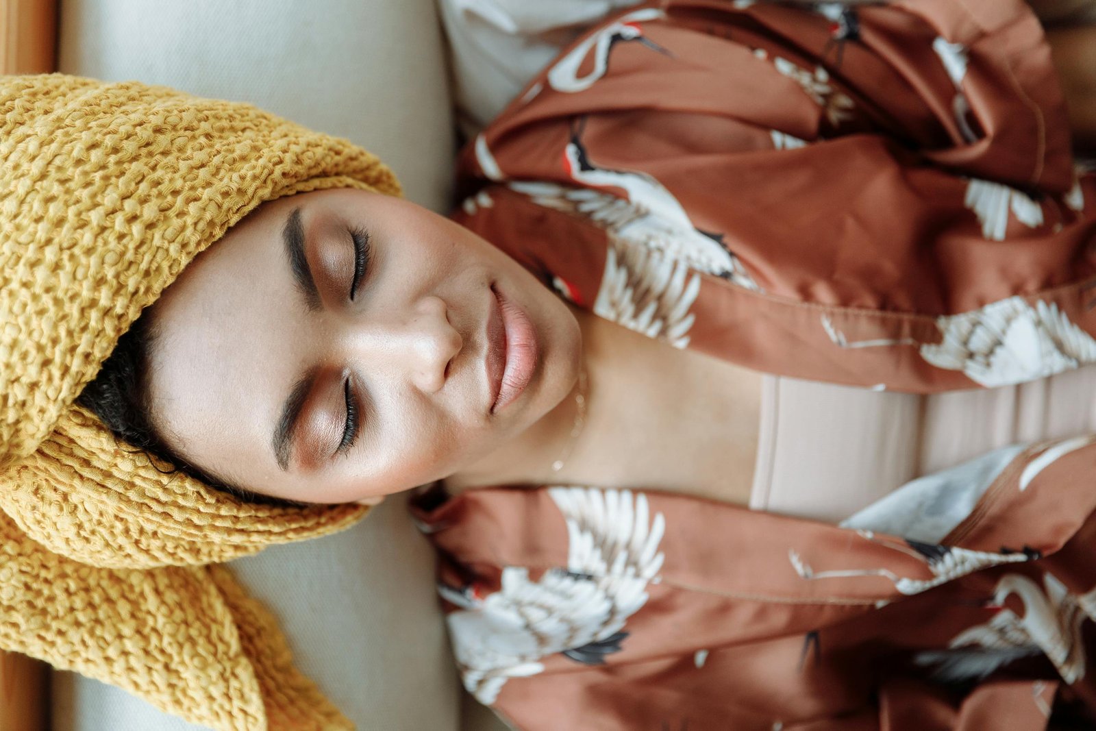 Peaceful woman with closed eyes, wearing a towel and patterned robe indoors.
